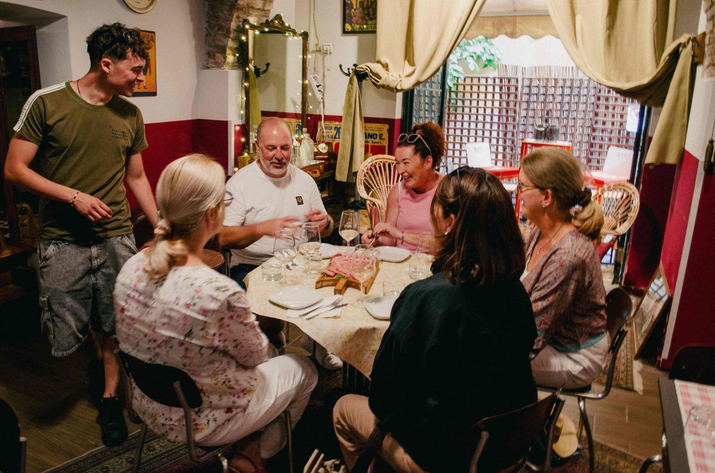 Guests sharing mortadella and wine at a table in a traditional osteria, with their guide